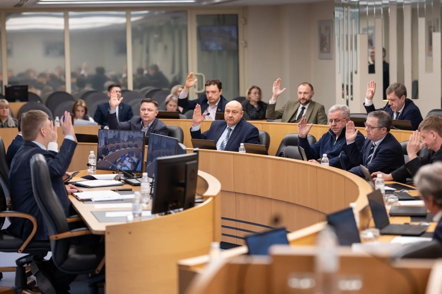 Депутаты в зале заседаний голосуют по вопросу повестки дня поднятием руки